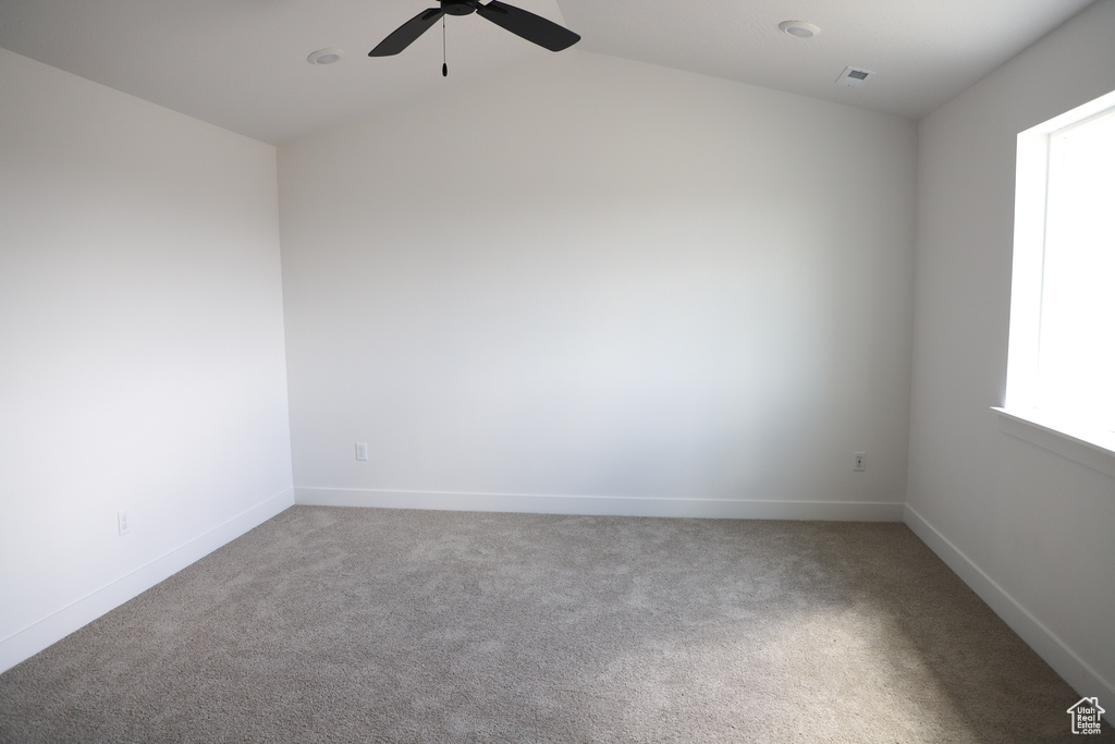 Carpeted empty room featuring ceiling fan, baseboards, and vaulted ceiling