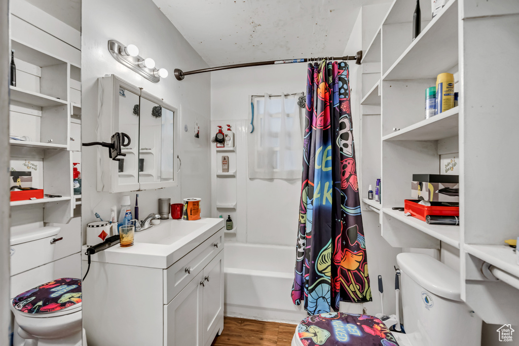 Bathroom with toilet, shower / bathtub combination with curtain, vanity, and wood finished floors