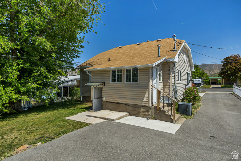 View of front of home with central AC unit, a front yard, entry steps, and roof with shingles