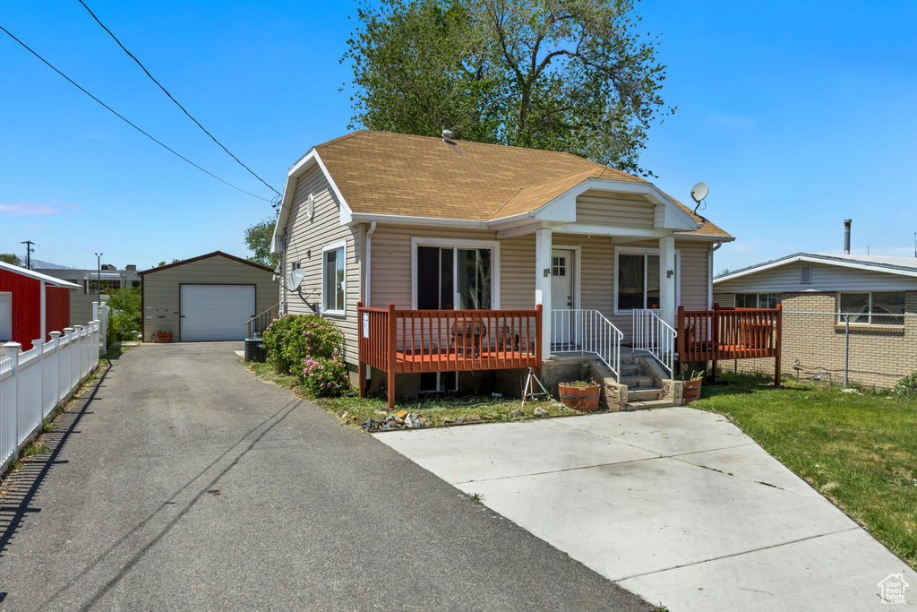 Bungalow-style home with asphalt driveway, a garage, a shingled roof, an outbuilding, and covered porch