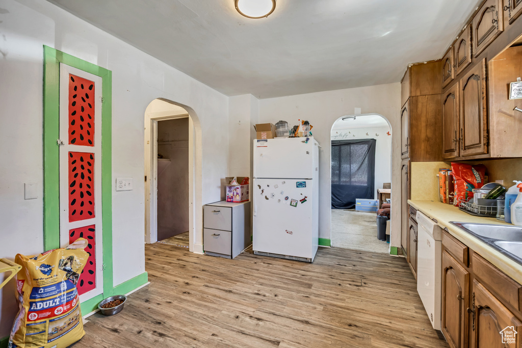 Kitchen with white appliances, arched walkways, light wood finished floors, brown cabinets, and light countertops