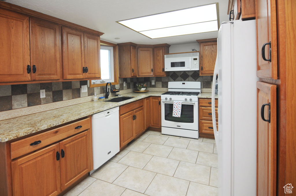Kitchen featuring white appliances, a sink, brown cabinetry, and decorative backsplash