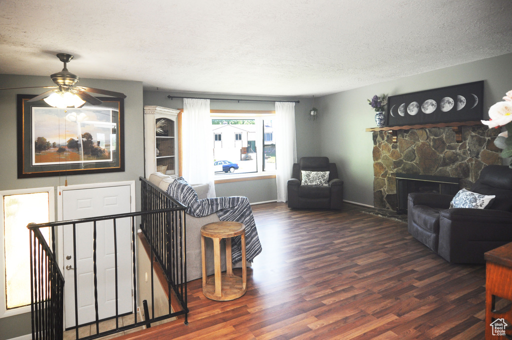 Living room with wood finished floors, a textured ceiling, a ceiling fan, baseboards, and a stone fireplace