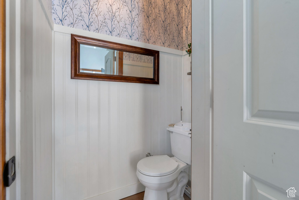 Bathroom with wallpapered walls, toilet, a decorative wall, and a wainscoted wall