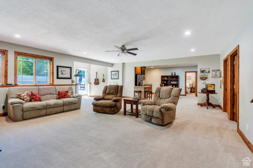 Living room featuring light carpet, recessed lighting, a textured ceiling, a ceiling fan, and baseboards