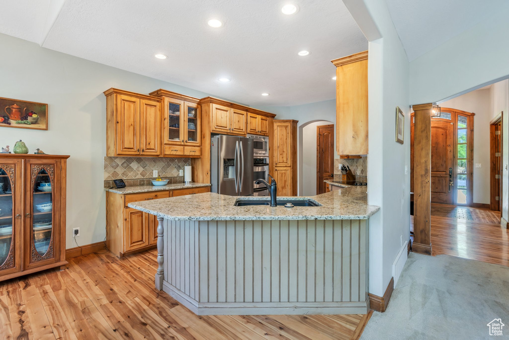 Kitchen featuring stainless steel appliances, arched walkways, a sink, light wood-style floors, and light stone counters