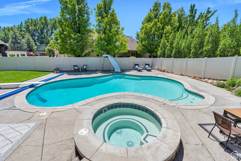 View of pool featuring an in-ground hot tub, a water slide, a fenced backyard, and a patio area