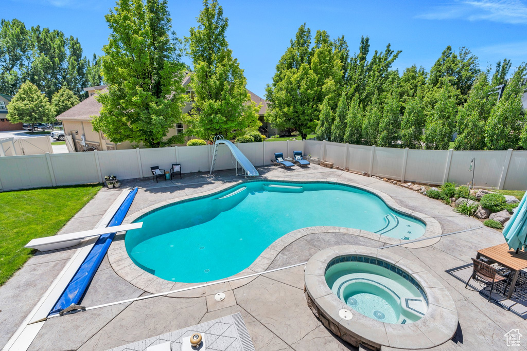 View of swimming pool featuring a water slide, an in-ground hot tub, a diving board, a patio, and a fenced backyard