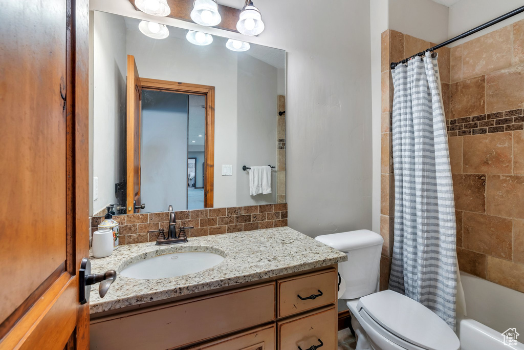 Bathroom featuring vanity, toilet, shower / bath combo, and backsplash