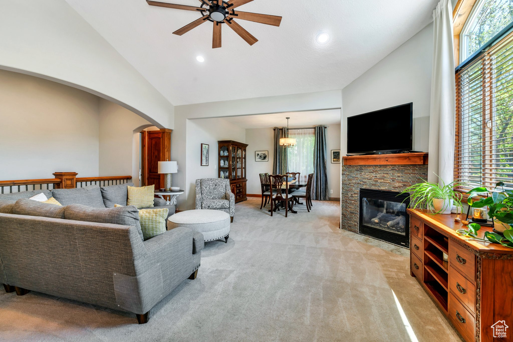 Living room featuring a ceiling fan, high vaulted ceiling, light colored carpet, arched walkways, and a fireplace