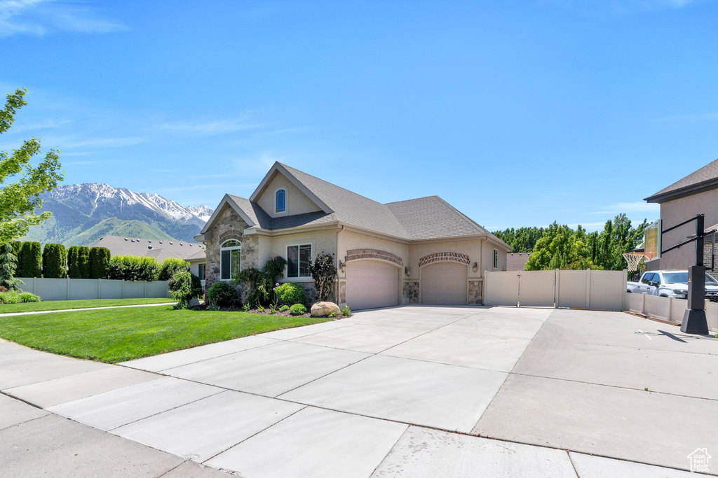 View of front of property with stone siding, a garage, stucco siding, a mountain view, and concrete driveway
