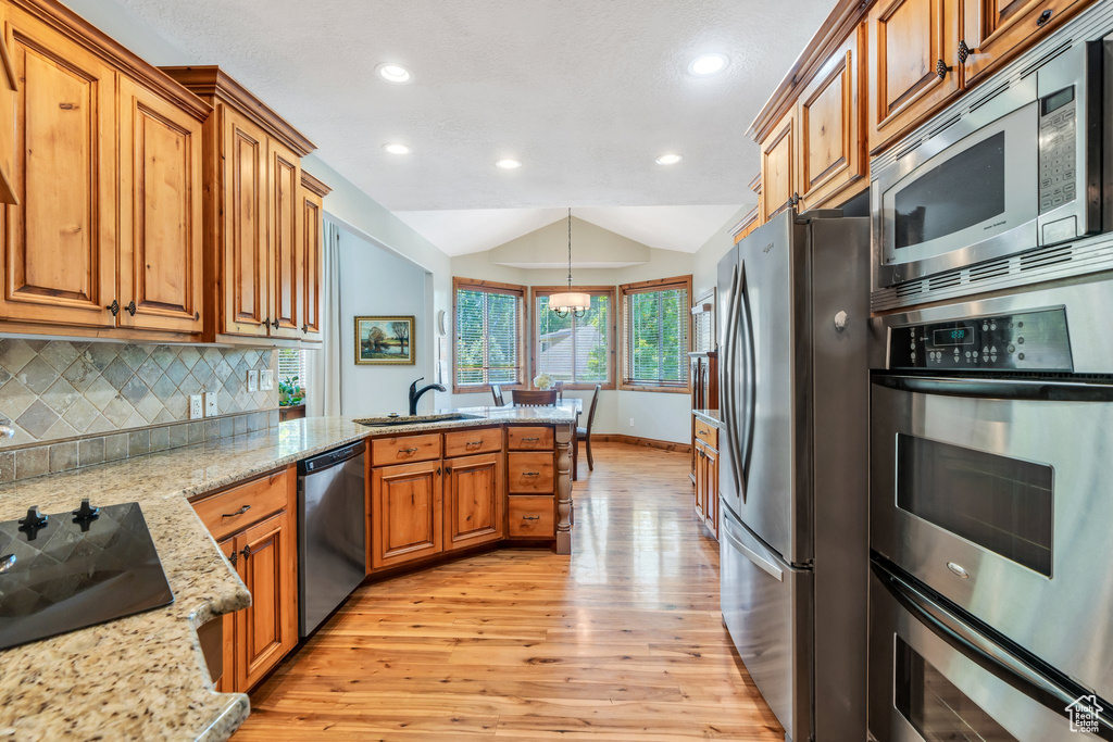 Kitchen featuring stainless steel appliances, light wood-style floors, a sink, a peninsula, and vaulted ceiling