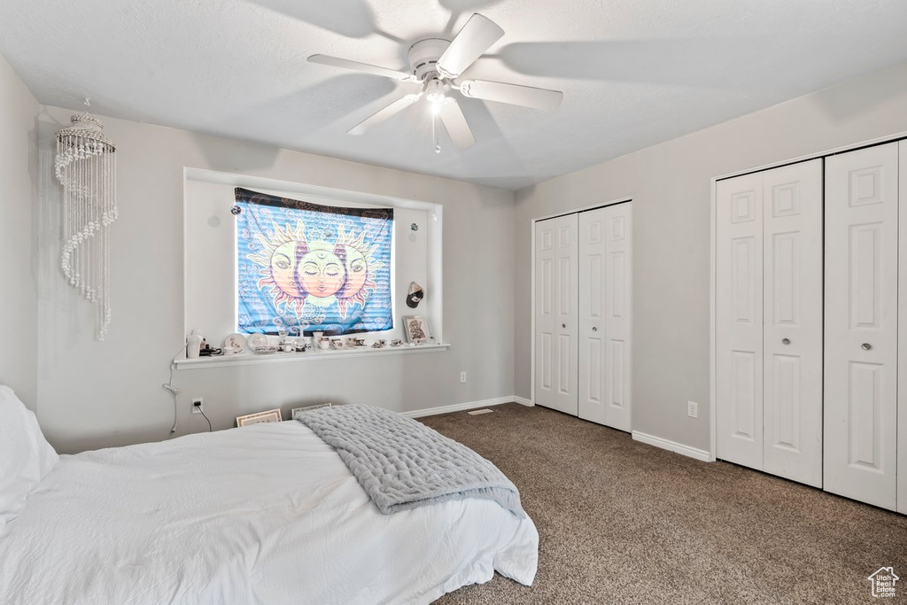 Carpeted bedroom with two closets, baseboards, and ceiling fan