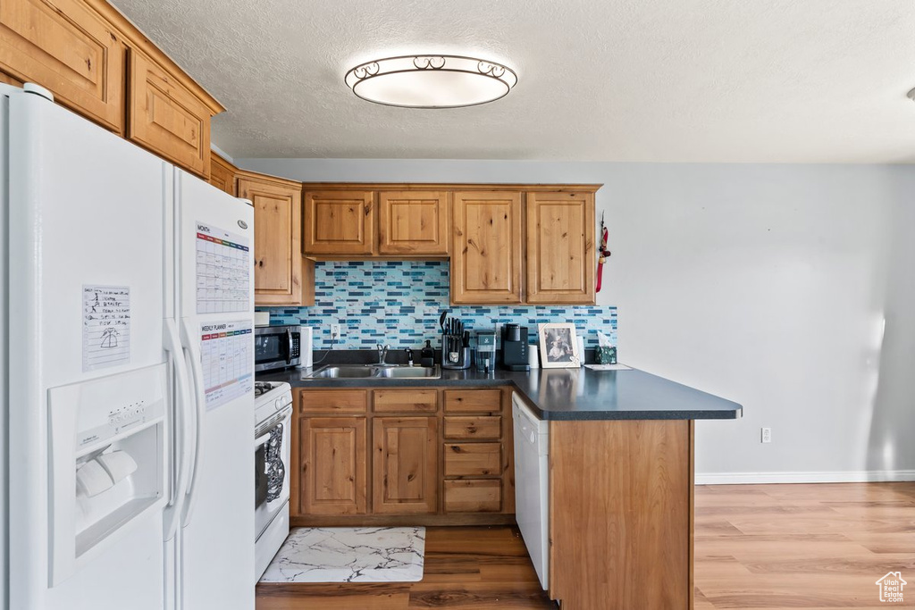 Kitchen with white appliances, a sink, dark countertops, a peninsula, and tasteful backsplash