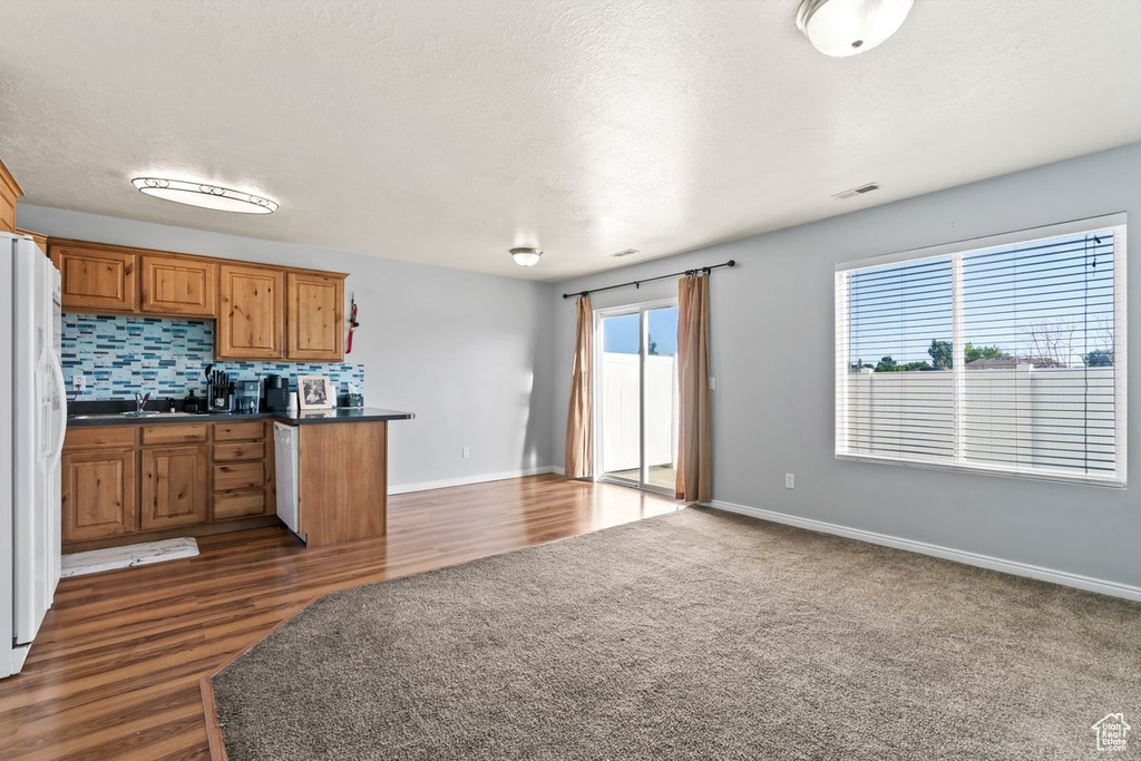 Kitchen featuring dark countertops, white fridge with ice dispenser, brown cabinets, open floor plan, and backsplash