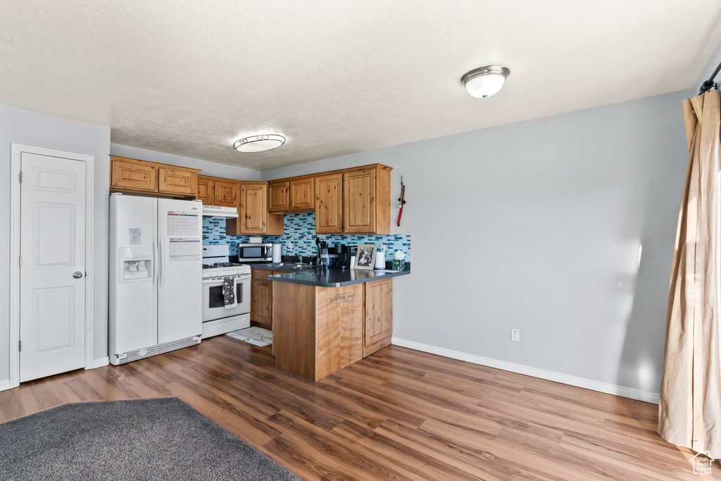 Kitchen with white appliances, a peninsula, under cabinet range hood, wood finished floors, and baseboards