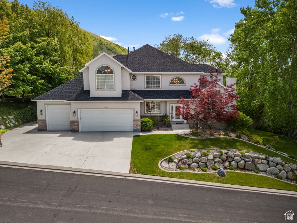 Traditional-style house with stucco siding, a front yard, concrete driveway, and a shingled roof