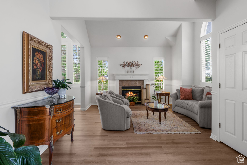 Living area with wood finished floors, a tile fireplace, vaulted ceiling, recessed lighting, and baseboards