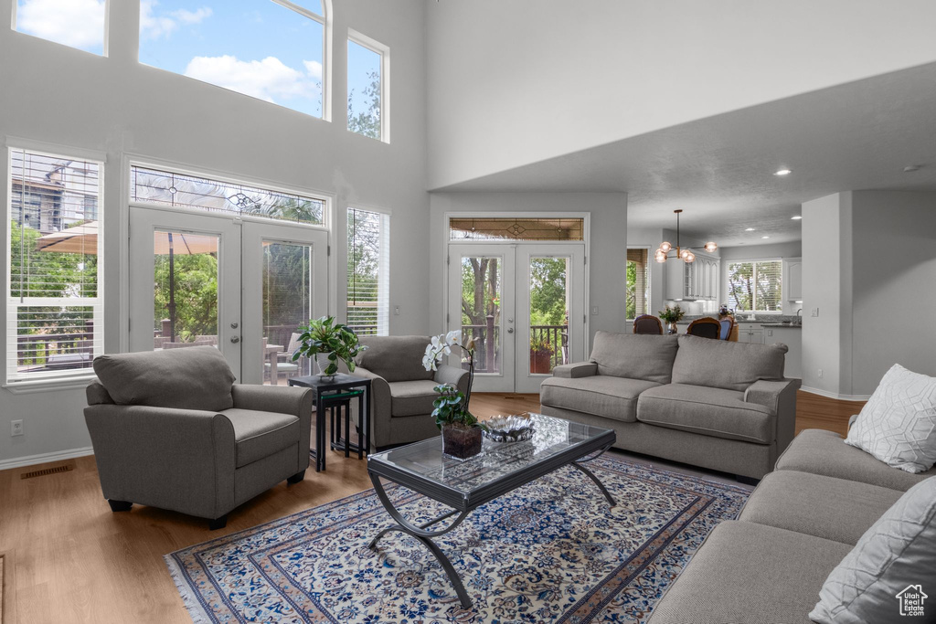 Living area featuring french doors, a chandelier, wood finished floors, baseboards, and a towering ceiling