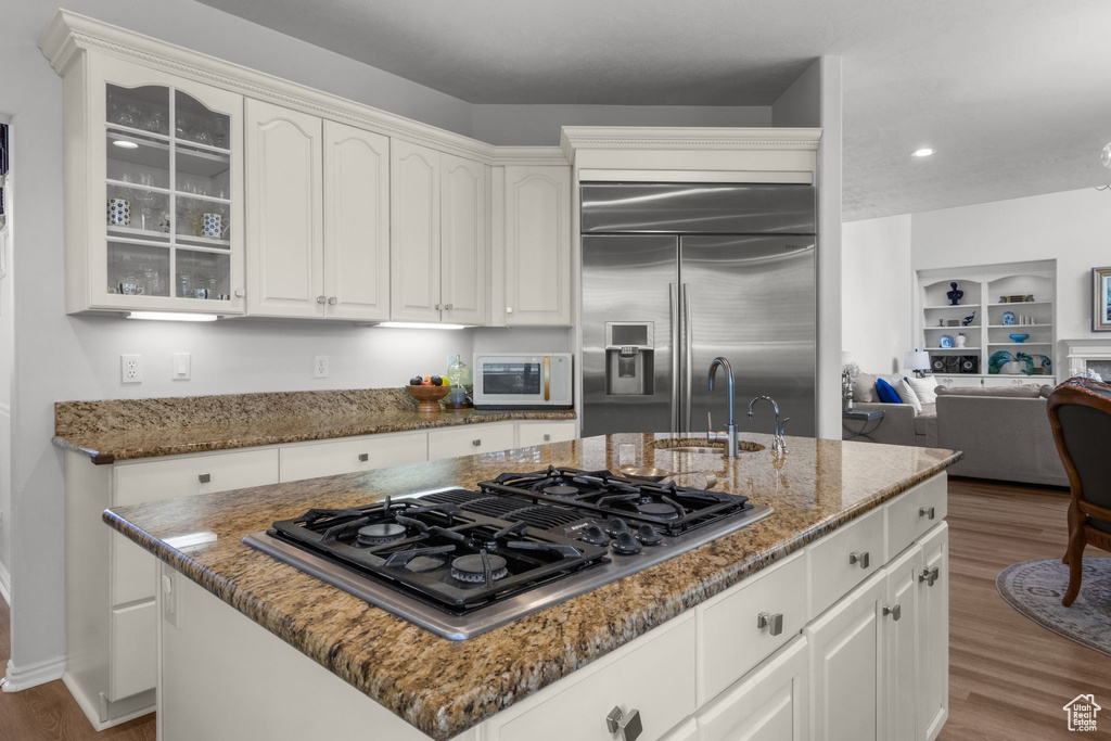 Kitchen featuring stovetop with downdraft, white microwave, a sink, built in fridge, and wood finished floors