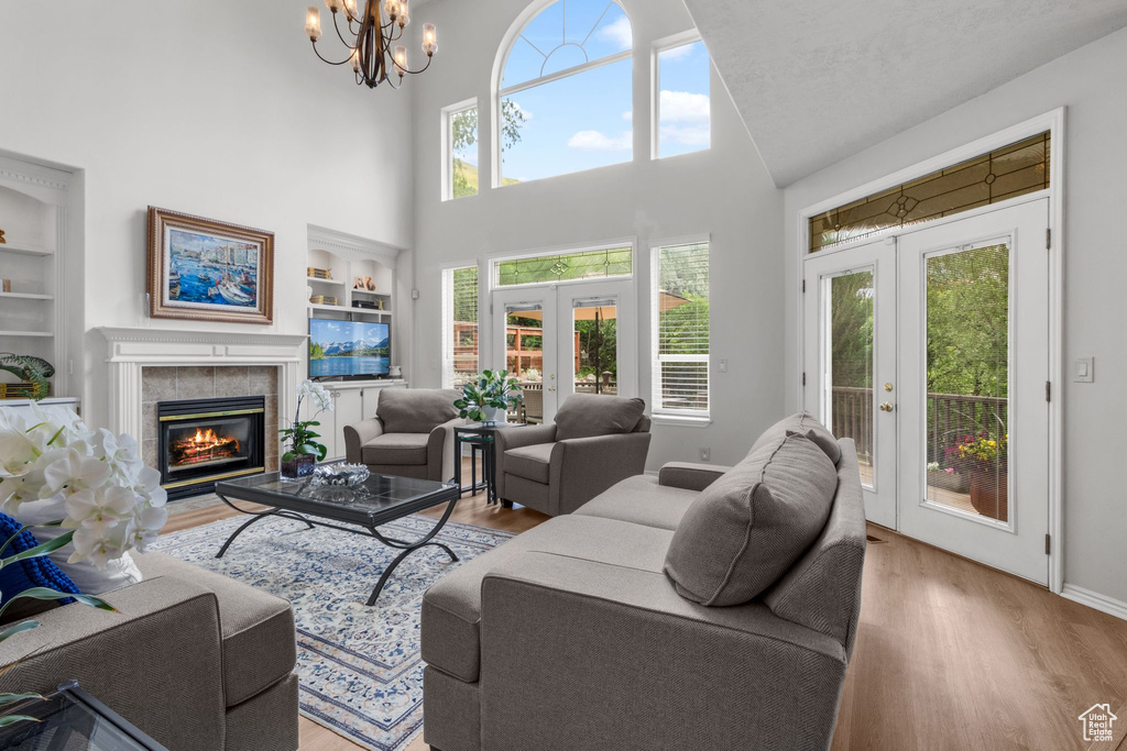 Living room with french doors, built in shelves, a tiled fireplace, wood finished floors, and healthy amount of natural light