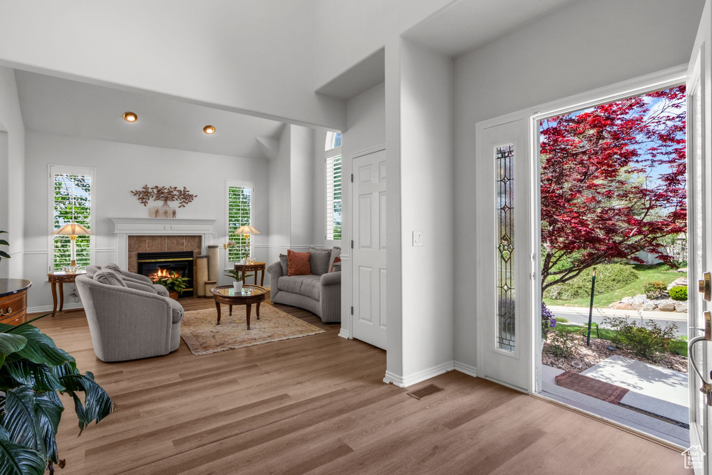 Entryway featuring light wood-type flooring, a tiled fireplace, baseboards, recessed lighting, and a high ceiling