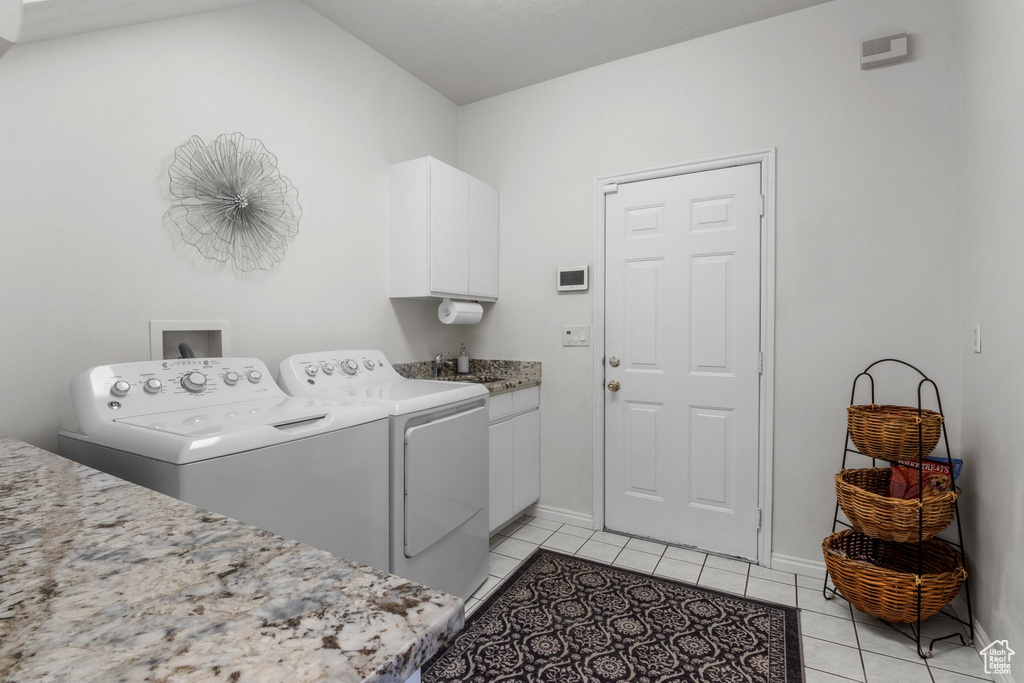 Laundry room with washing machine and clothes dryer, light tile patterned flooring, cabinet space, and baseboards