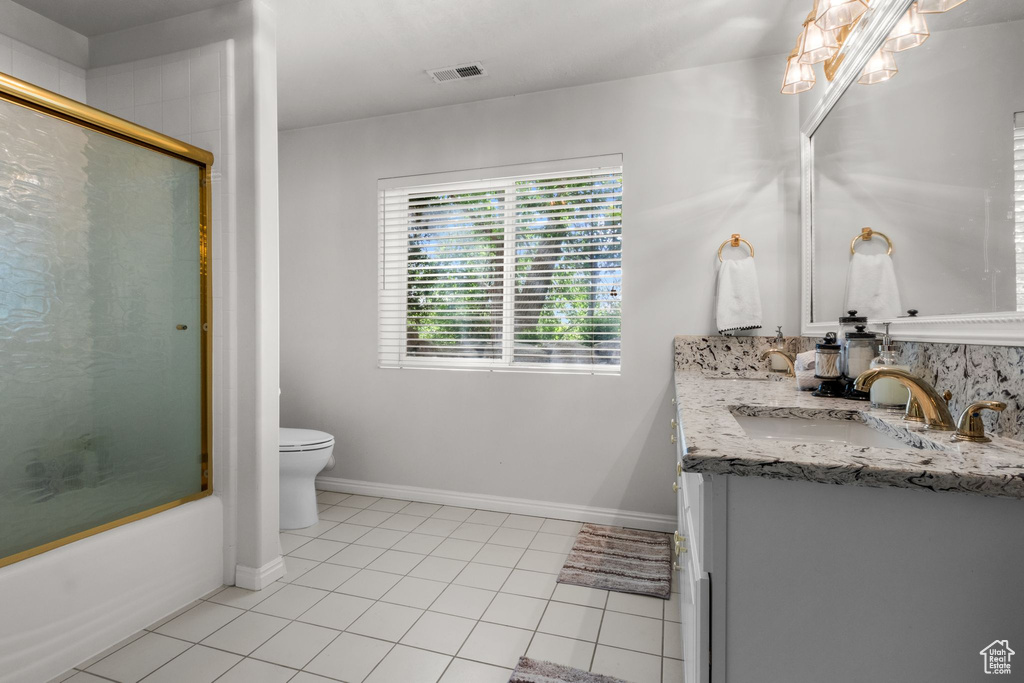Full bath with toilet, tile patterned floors, vanity, combined bath / shower with glass door, and baseboards