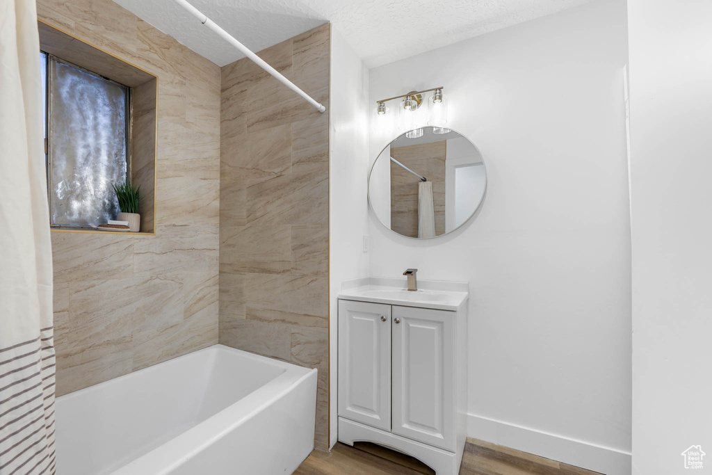 Full bathroom with vanity, shower / tub combo with curtain, wood finished floors, baseboards, and a textured ceiling