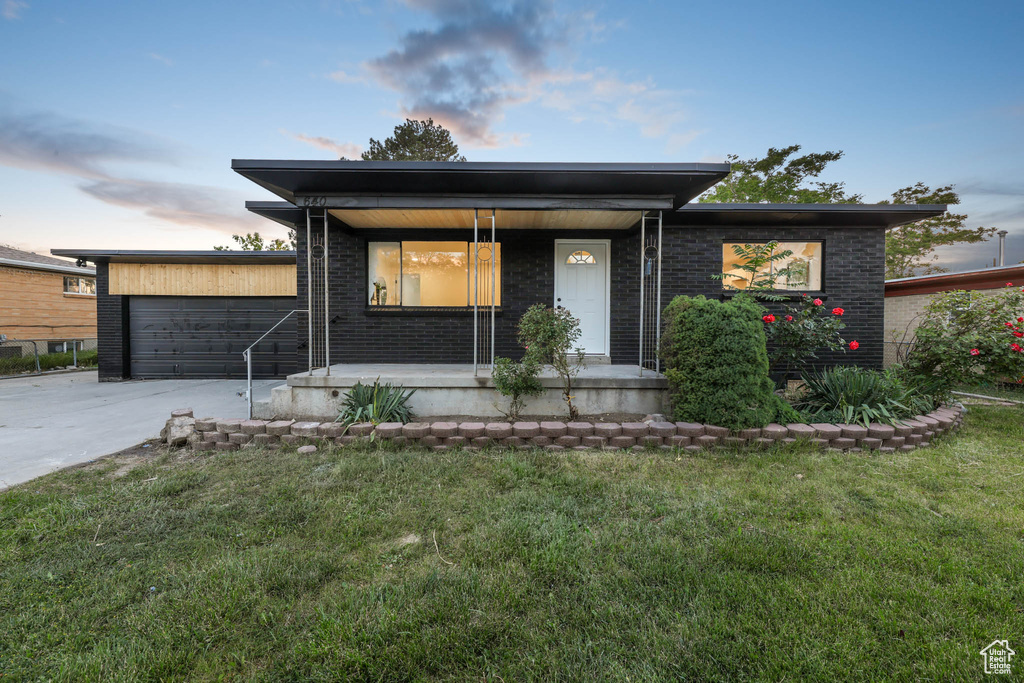 View of front of home featuring concrete driveway, covered porch, a front yard, and brick siding