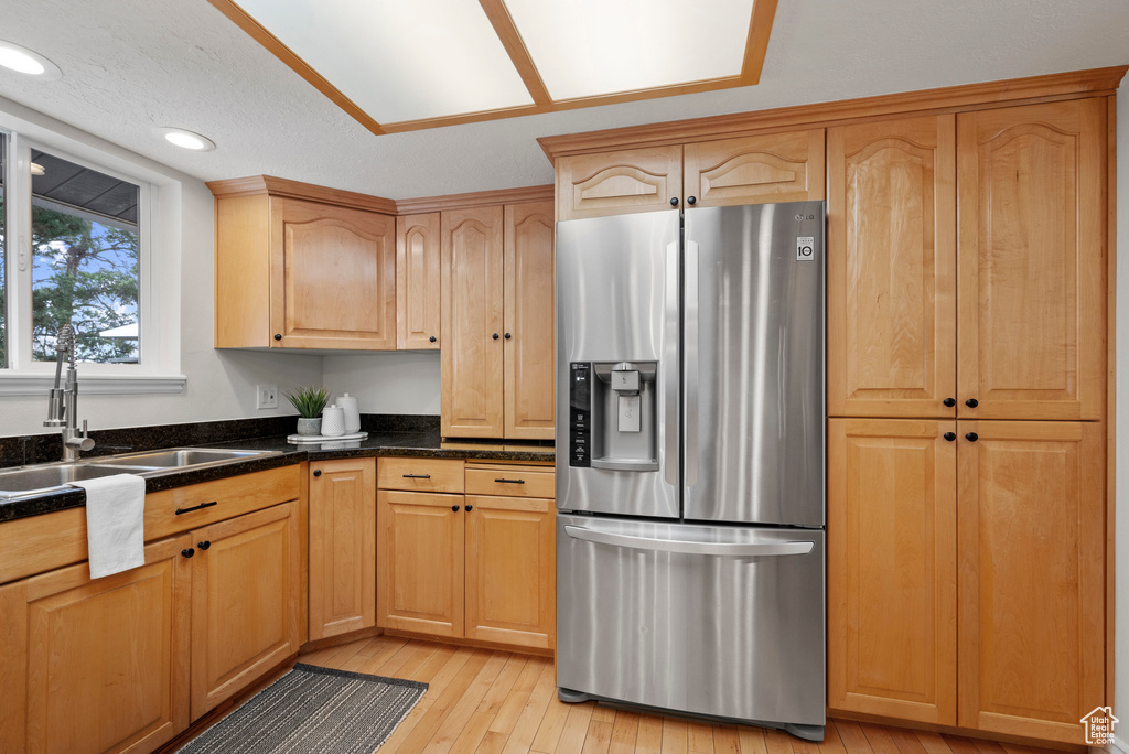 Kitchen with stainless steel fridge, a sink, light wood-type flooring, recessed lighting, and dark stone counters