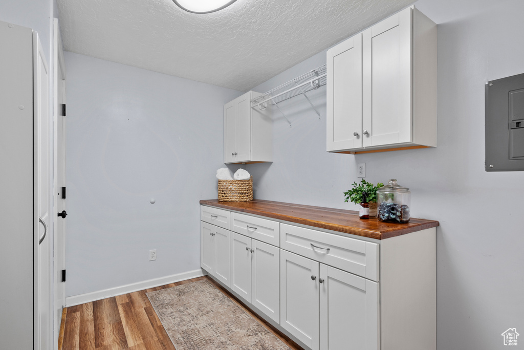 Washroom with light wood finished floors, electric panel, a textured ceiling, and baseboards