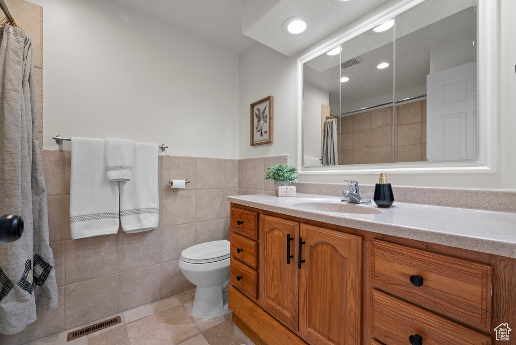 Bathroom featuring vanity, tile walls, tiled shower, tile patterned flooring, and toilet