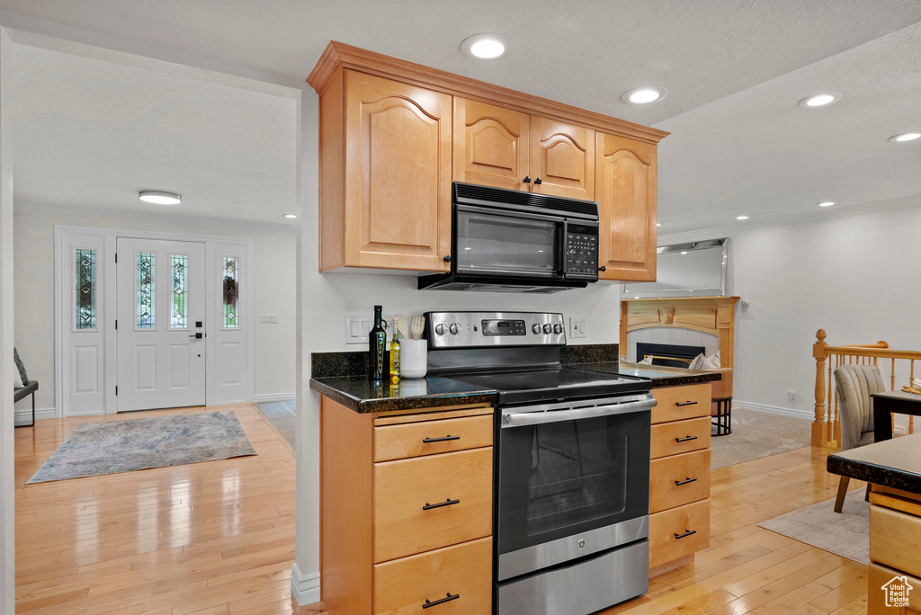 Kitchen with black microwave, stainless steel range with electric stovetop, baseboards, light wood-style flooring, and light brown cabinets
