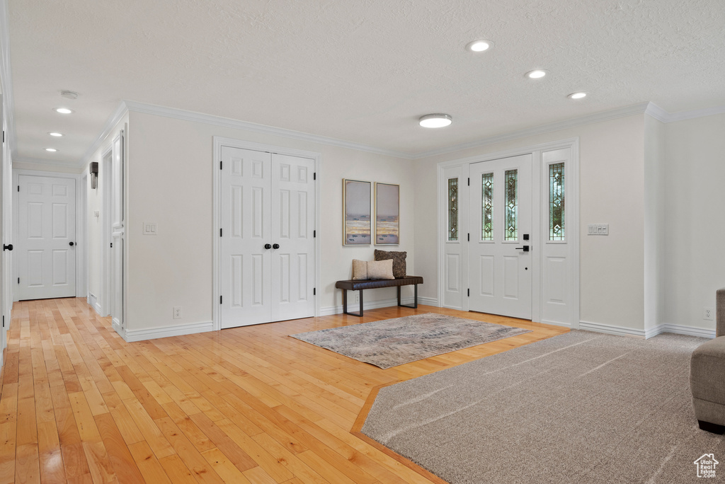 Entryway featuring crown molding, light wood-style floors, baseboards, recessed lighting, and a textured ceiling