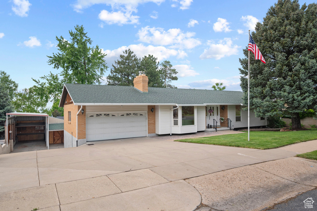Ranch-style home featuring an attached garage, a shingled roof, a front lawn, a chimney, and concrete driveway