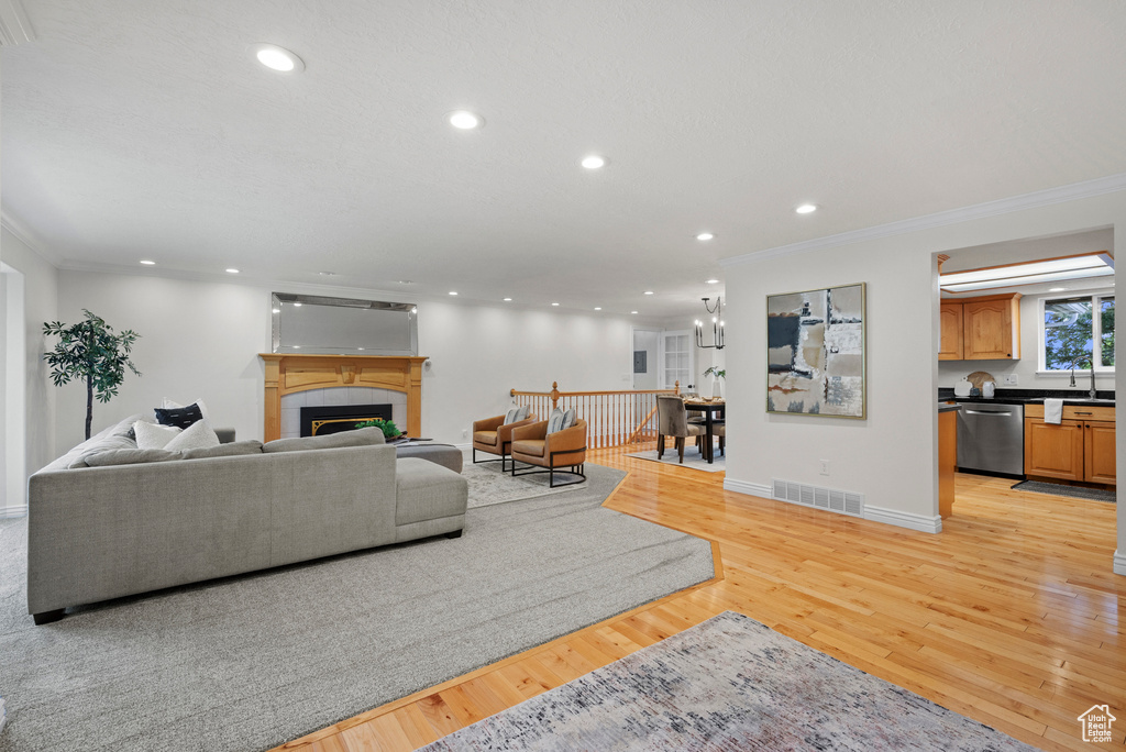 Living room featuring ornamental molding, recessed lighting, a tiled fireplace, light wood-type flooring, and baseboards