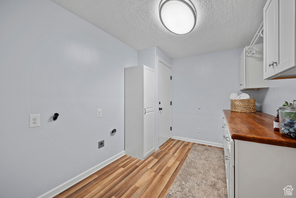 Laundry area featuring electric dryer hookup, light wood-style floors, a textured ceiling, baseboards, and cabinet space