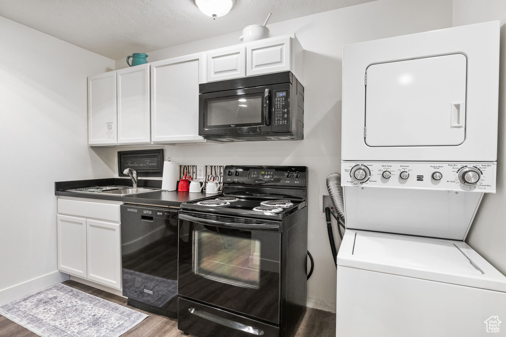 Kitchen with black appliances, stacked washer / dryer, a sink, wood finished floors, and white cabinets