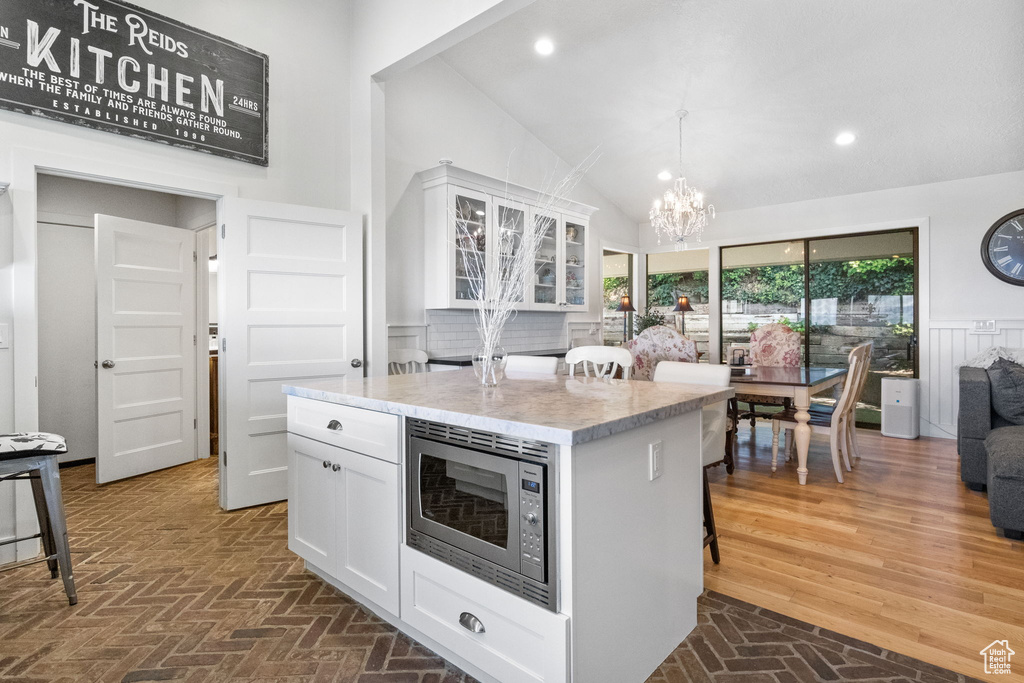 Kitchen featuring stainless steel microwave, white cabinetry, a chandelier, brick patterned flooring, and a center island