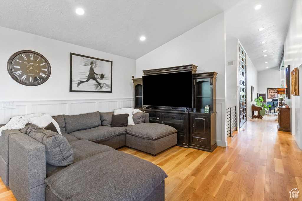 Living area featuring lofted ceiling, light wood-style floors, recessed lighting, wainscoting, and a decorative wall