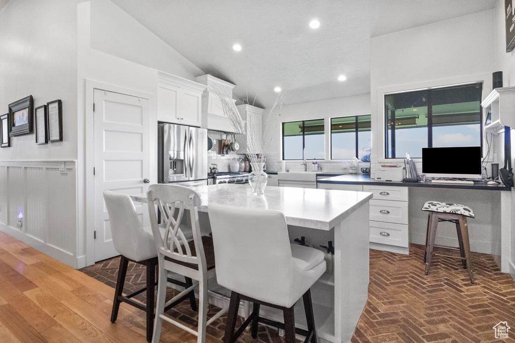 Kitchen featuring stainless steel fridge with ice dispenser, a kitchen breakfast bar, white cabinetry, a center island, and vaulted ceiling