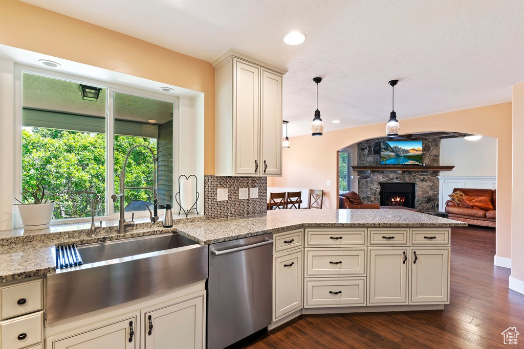 Kitchen featuring dishwasher, a peninsula, a stone fireplace, dark wood-style flooring, and light stone counters