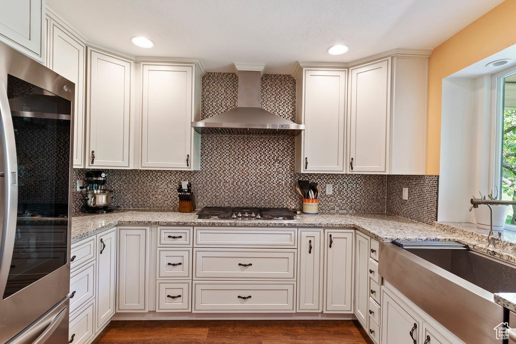 Kitchen with wall chimney exhaust hood, fridge, stainless steel gas stovetop, a sink, and backsplash