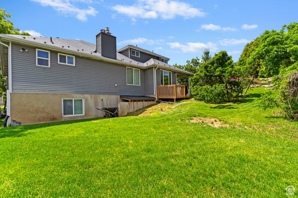 Back of house with a deck, a chimney, and a yard
