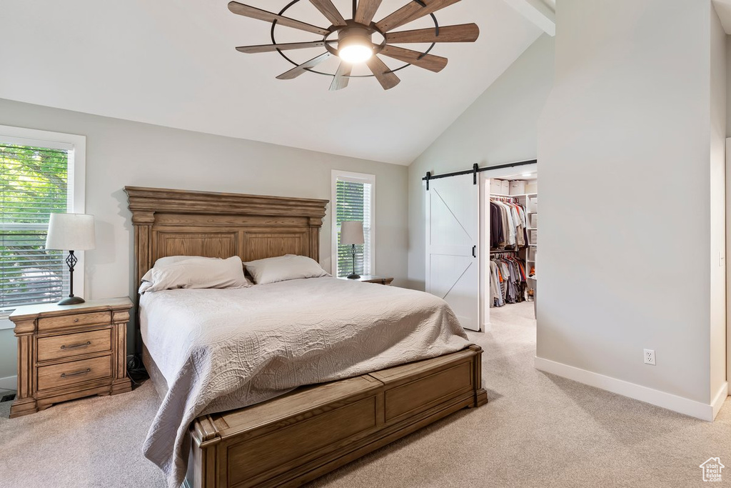 Bedroom featuring light carpet, a barn door, baseboards, a spacious closet, and ceiling fan
