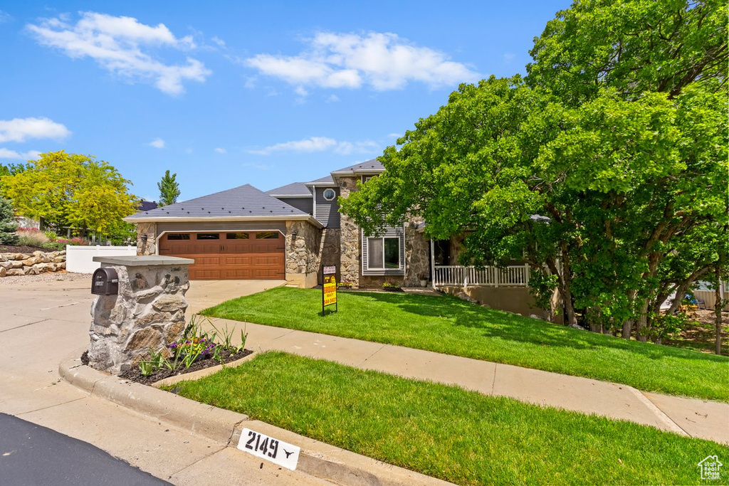 View of front of property featuring stone siding, an attached garage, concrete driveway, and a front yard