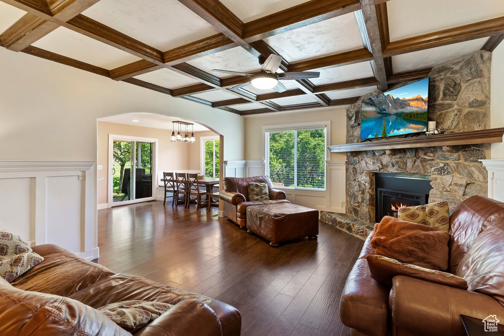 Living area with coffered ceiling, ceiling fan, a stone fireplace, arched walkways, and dark wood-type flooring