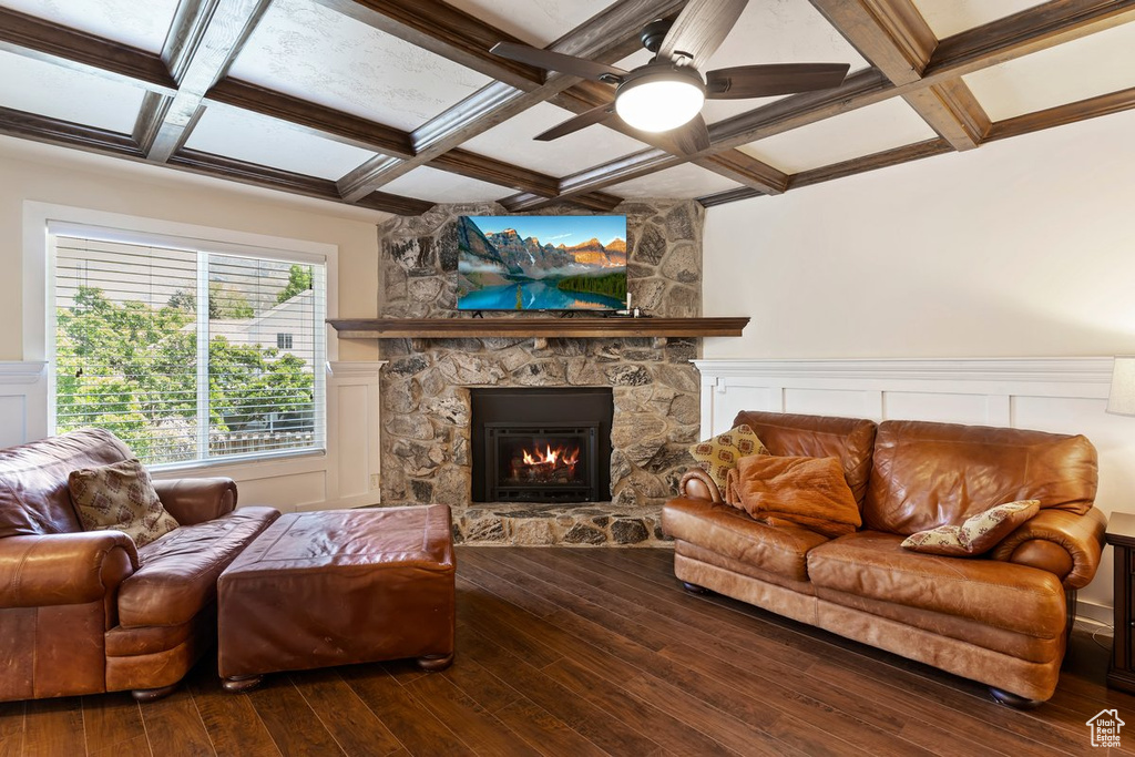 Living room with coffered ceiling, a stone fireplace, hardwood / wood-style floors, a ceiling fan, and beamed ceiling