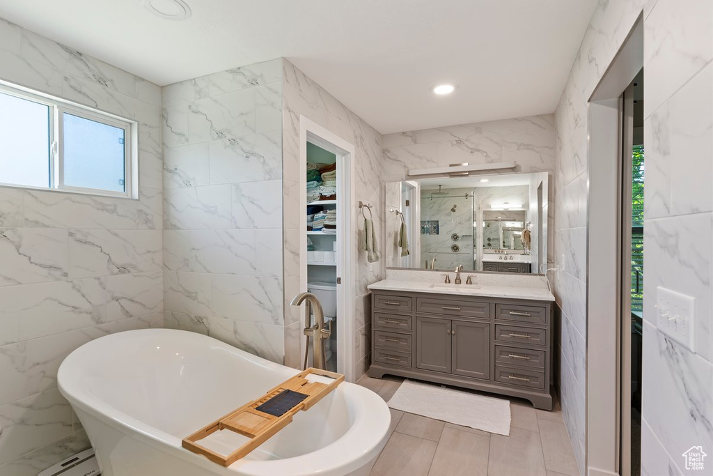 Full bathroom with tile walls, vanity, a soaking tub, a marble finish shower, and recessed lighting